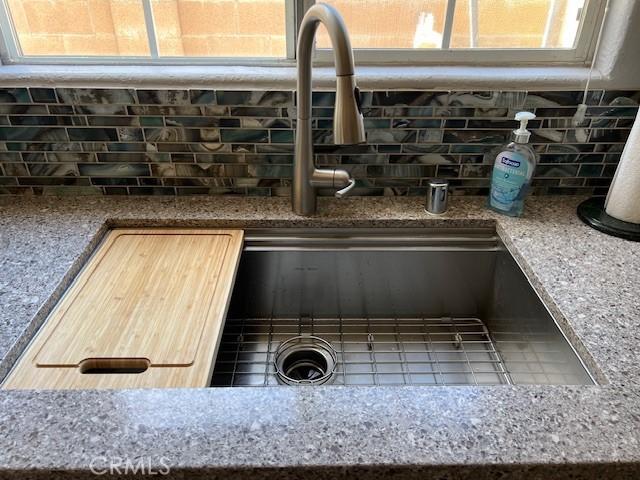 interior details featuring a sink, stone countertops, and backsplash