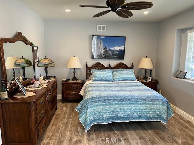 bedroom featuring a ceiling fan, baseboards, visible vents, and wood finished floors