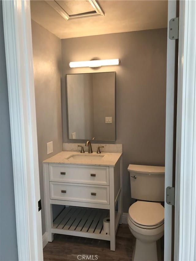 half bath featuring toilet, baseboards, wood finished floors, and vanity