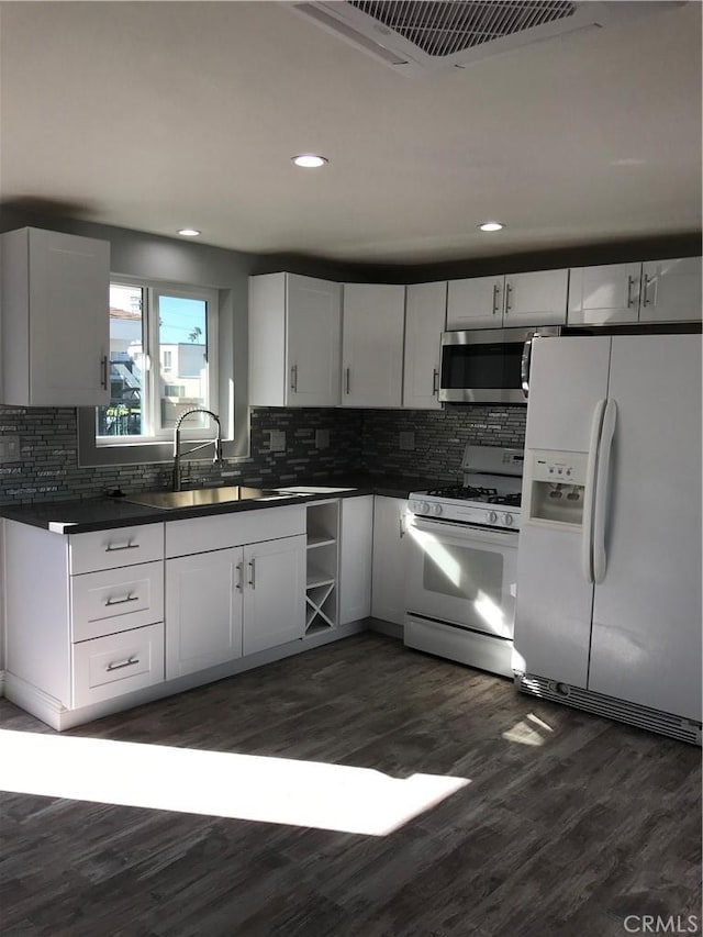 kitchen featuring white appliances, dark countertops, dark wood-style flooring, a sink, and backsplash