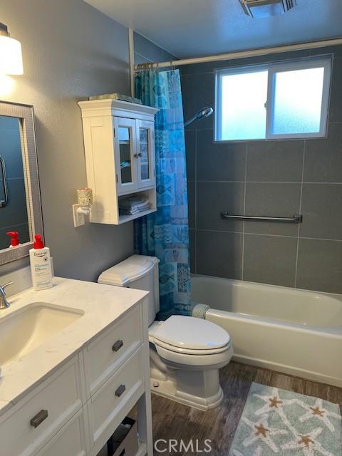 bathroom featuring vanity, shower / bathtub combination with curtain, toilet, and wood finished floors