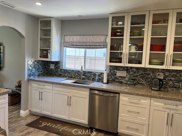 kitchen with arched walkways, wood finished floors, a sink, backsplash, and dishwasher