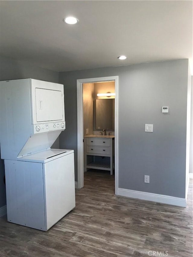 laundry area featuring dark wood finished floors, stacked washer / drying machine, recessed lighting, a sink, and baseboards