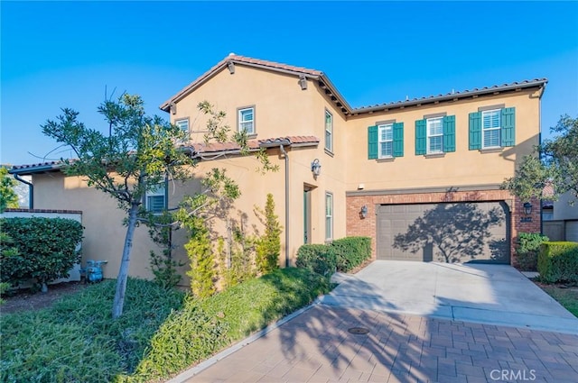 mediterranean / spanish-style house featuring brick siding, a tile roof, stucco siding, decorative driveway, and a garage