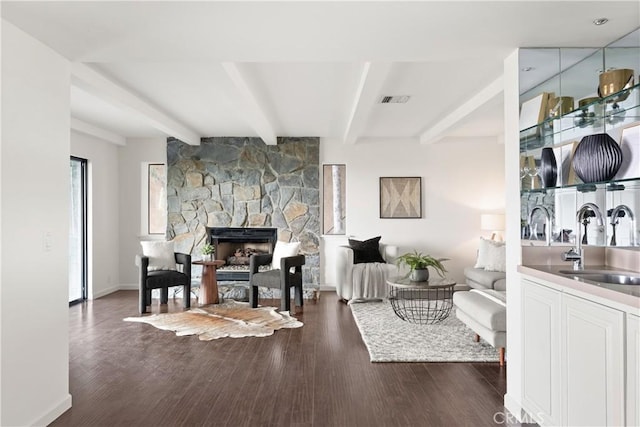 living area featuring dark wood-type flooring, beam ceiling, visible vents, and a stone fireplace