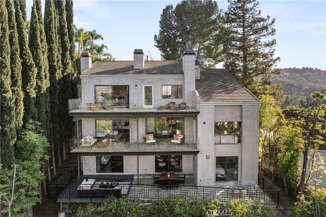 back of property with stucco siding, a balcony, and a chimney