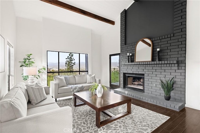 living room featuring high vaulted ceiling, beamed ceiling, a brick fireplace, and wood finished floors