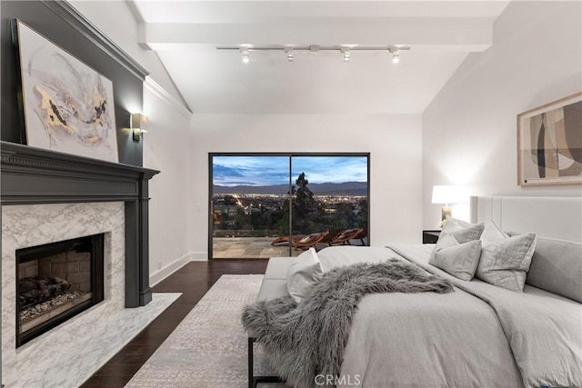 bedroom with baseboards, dark wood finished floors, lofted ceiling, a premium fireplace, and rail lighting