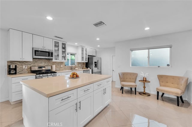 kitchen featuring tasteful backsplash, visible vents, glass insert cabinets, appliances with stainless steel finishes, and light countertops