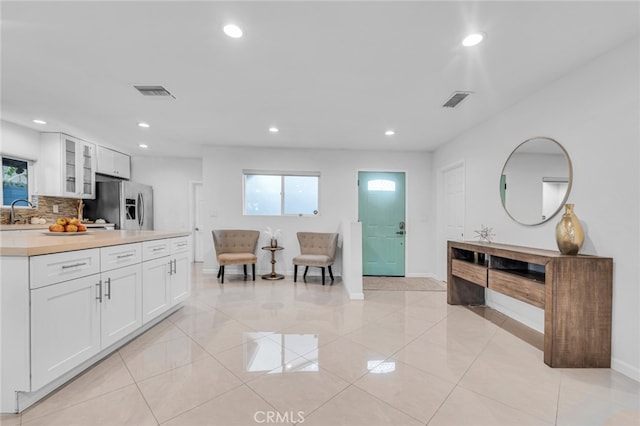 kitchen with a sink, visible vents, white cabinetry, stainless steel refrigerator with ice dispenser, and tasteful backsplash