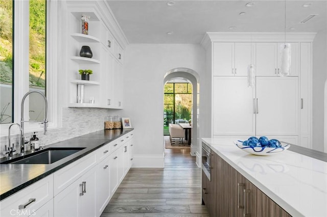 kitchen featuring arched walkways, open shelves, decorative backsplash, a sink, and wood finished floors