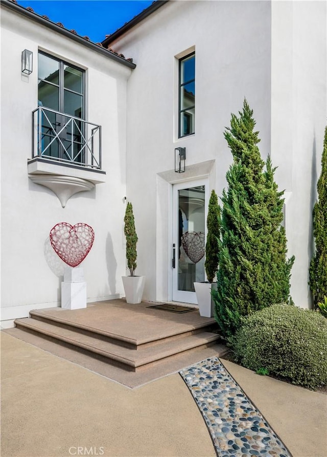 view of exterior entry with a balcony and stucco siding