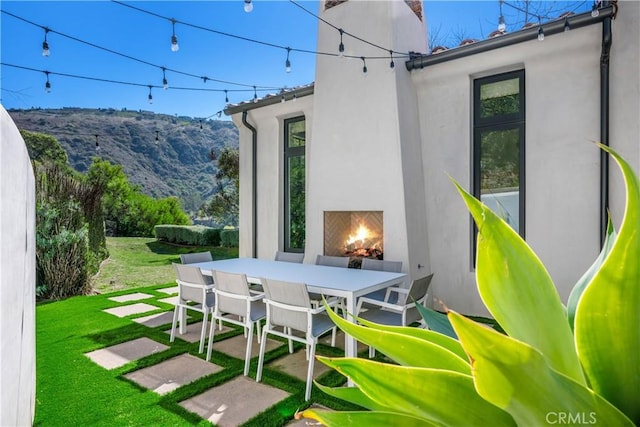 view of patio / terrace with outdoor dining space, a mountain view, and a lit fireplace