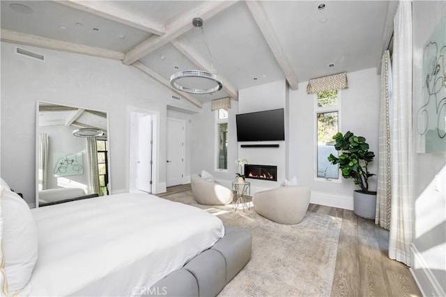 bedroom with baseboards, visible vents, a glass covered fireplace, lofted ceiling with beams, and wood finished floors