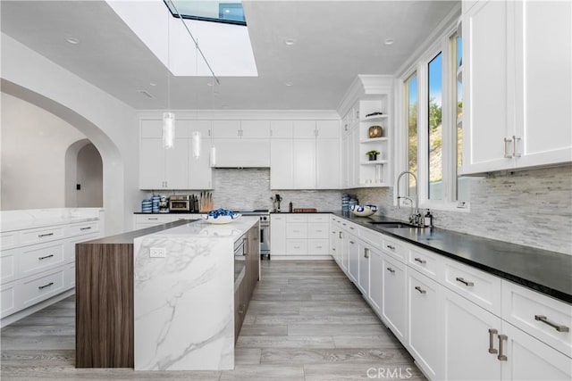 kitchen with light wood-style floors, a skylight, a sink, and white cabinets