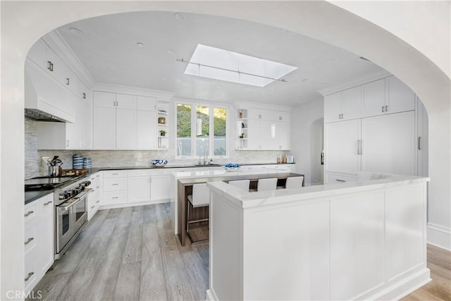 kitchen with range with two ovens, a kitchen island, light wood-type flooring, decorative backsplash, and open shelves