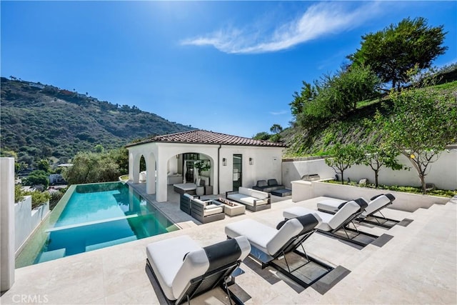 view of swimming pool with a patio, an outdoor living space with a fire pit, a fenced backyard, an infinity pool, and a gazebo