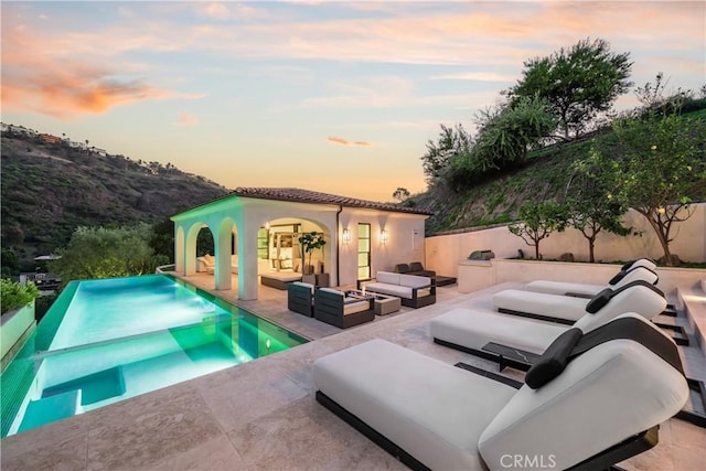 view of pool featuring an infinity pool, a patio, outdoor lounge area, fence, and an outdoor structure