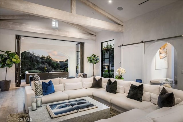 living area with arched walkways, wood finished floors, lofted ceiling with beams, and a barn door