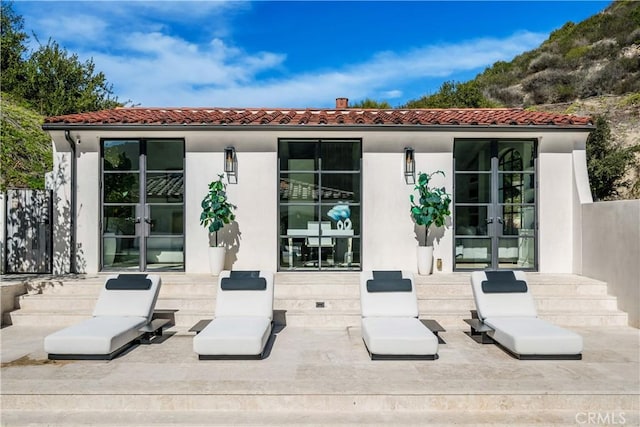 rear view of house featuring french doors, a tile roof, and stucco siding