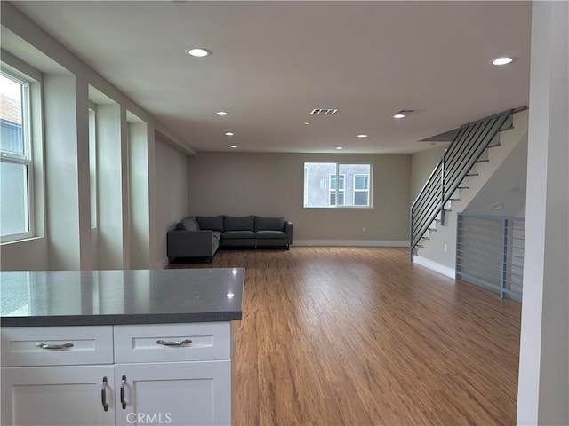 unfurnished living room with stairs, plenty of natural light, visible vents, and light wood finished floors