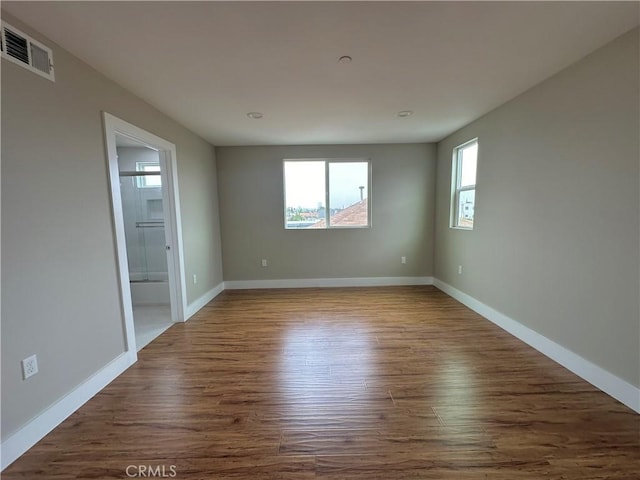 empty room featuring dark wood-type flooring, visible vents, and baseboards