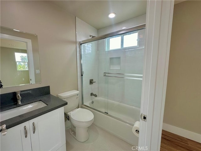 bathroom with vanity, toilet, baseboards, and bath / shower combo with glass door