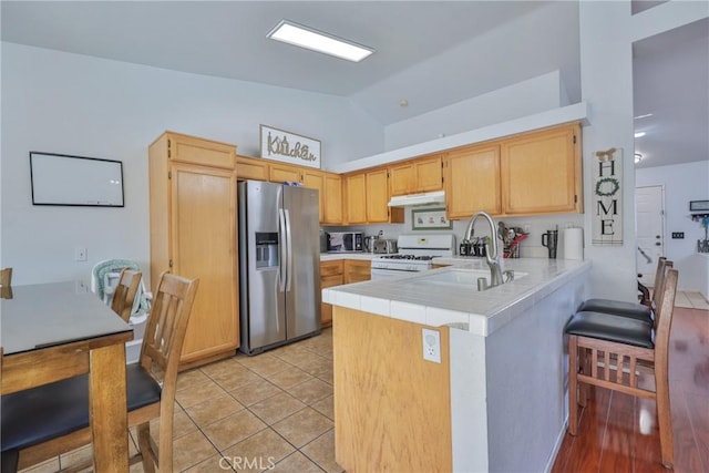 kitchen featuring under cabinet range hood, a peninsula, a sink, stainless steel fridge with ice dispenser, and gas range gas stove