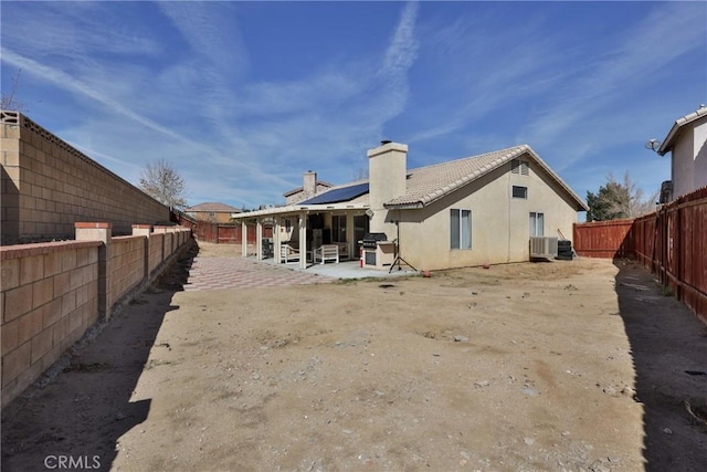 back of property featuring solar panels, a chimney, a patio area, and a fenced backyard