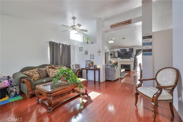 living room featuring a ceiling fan, high vaulted ceiling, a tiled fireplace, and wood finished floors