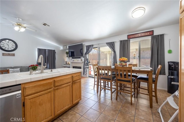 kitchen featuring a sink, visible vents, vaulted ceiling, tile counters, and dishwasher