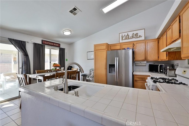 kitchen featuring white gas stove, tile counters, black microwave, stainless steel fridge, and under cabinet range hood