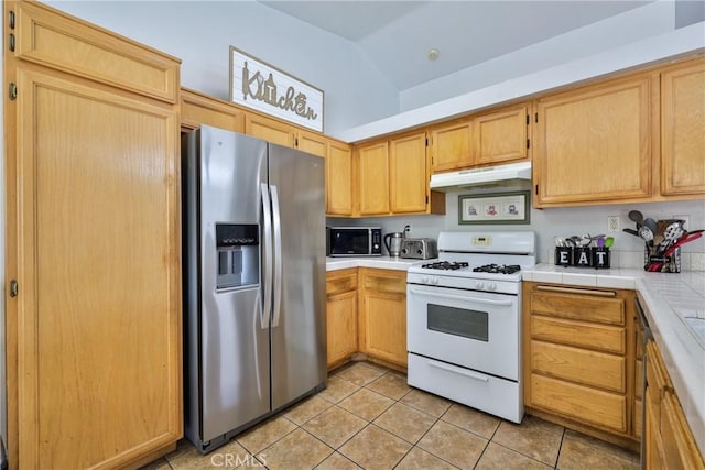 kitchen with light tile patterned floors, stainless steel fridge, vaulted ceiling, under cabinet range hood, and gas range gas stove