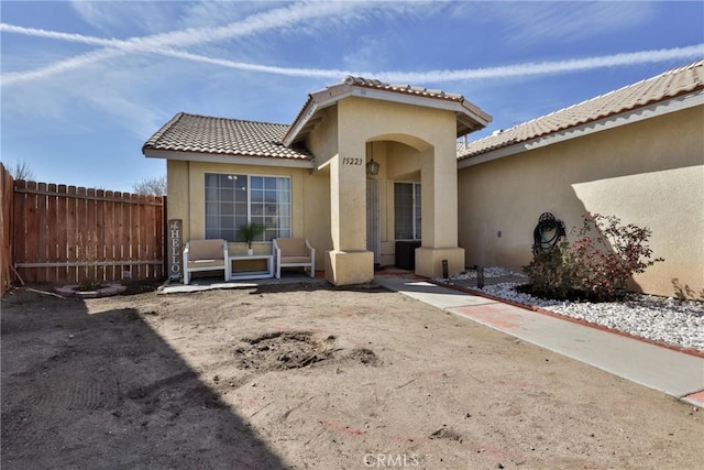 rear view of house featuring a tiled roof, fence, and stucco siding