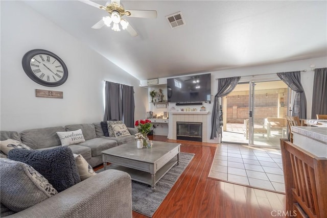 living area with visible vents, a ceiling fan, a tile fireplace, wood finished floors, and vaulted ceiling