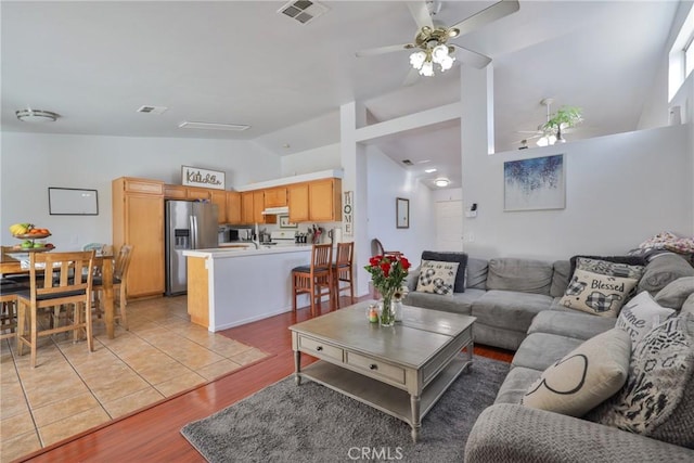 living room featuring lofted ceiling, visible vents, ceiling fan, and light wood-style flooring