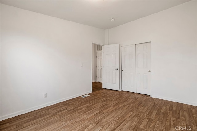 unfurnished bedroom featuring baseboards, visible vents, a closet, and wood finished floors