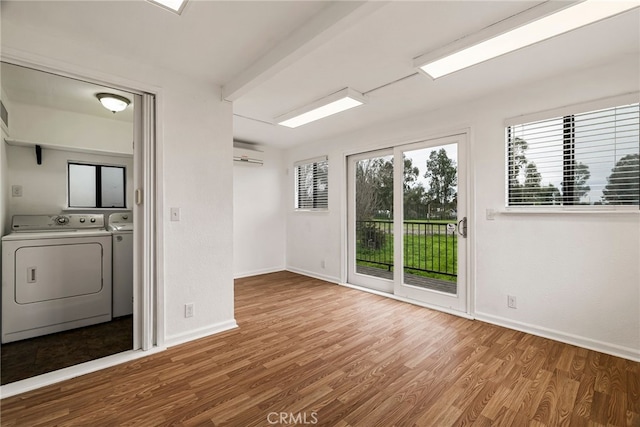 unfurnished room with a wall mounted AC, washer and clothes dryer, baseboards, and wood finished floors