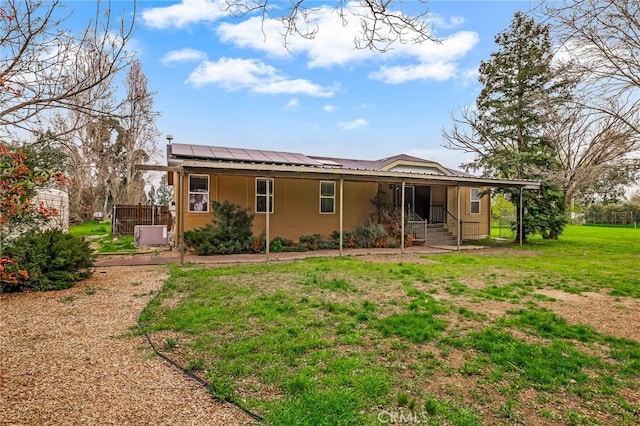 back of property with covered porch, stucco siding, a yard, and roof mounted solar panels