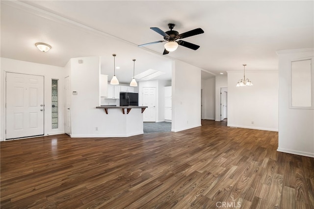 unfurnished living room featuring dark wood-type flooring, lofted ceiling, baseboards, and ceiling fan with notable chandelier