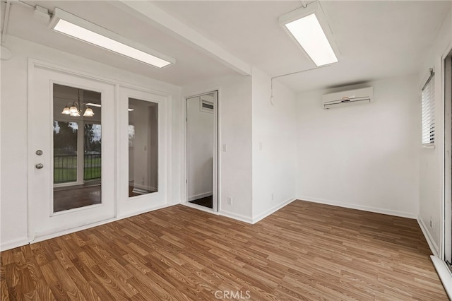 empty room featuring baseboards, a wall mounted AC, wood finished floors, and an inviting chandelier