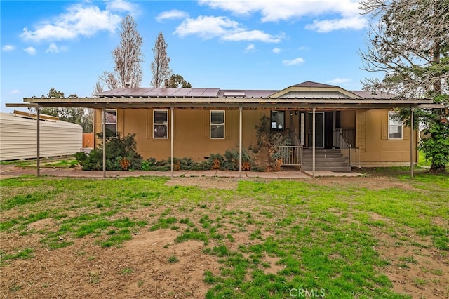 rear view of house featuring roof mounted solar panels, a lawn, entry steps, and metal roof
