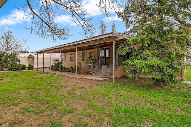 rear view of property featuring a lawn, a carport, and an outdoor structure