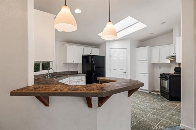 kitchen with a peninsula, a breakfast bar, dark countertops, a sink, and black appliances