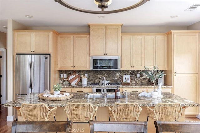 kitchen featuring a breakfast bar area, visible vents, light brown cabinetry, decorative backsplash, and appliances with stainless steel finishes