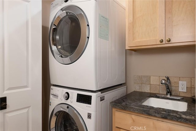 washroom featuring cabinet space, stacked washer and clothes dryer, and a sink