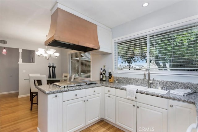 kitchen with custom exhaust hood, white cabinets, and a peninsula