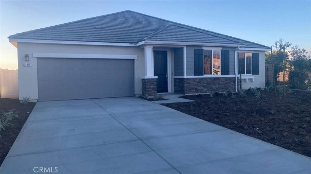 view of front of house with a garage, concrete driveway, stone siding, and a tiled roof