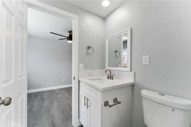 bathroom featuring toilet, wood finished floors, vanity, baseboards, and a ceiling fan