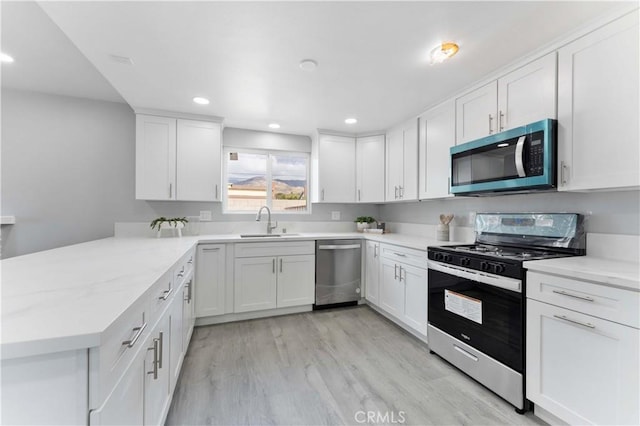 kitchen featuring light wood-style flooring, appliances with stainless steel finishes, white cabinetry, a sink, and a peninsula